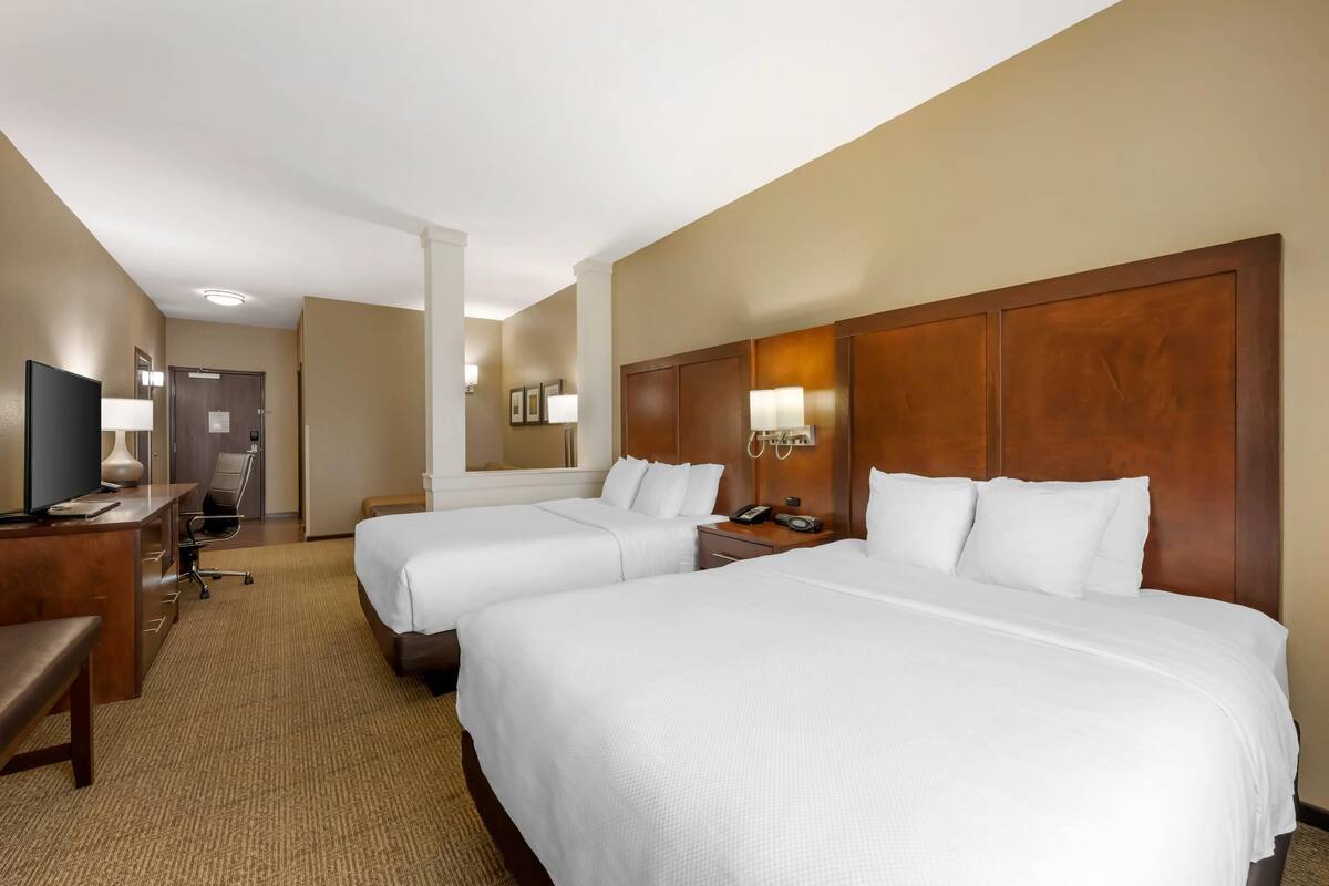 A hotel room with two beds, a desk with a chair, a TV, and a lamp.