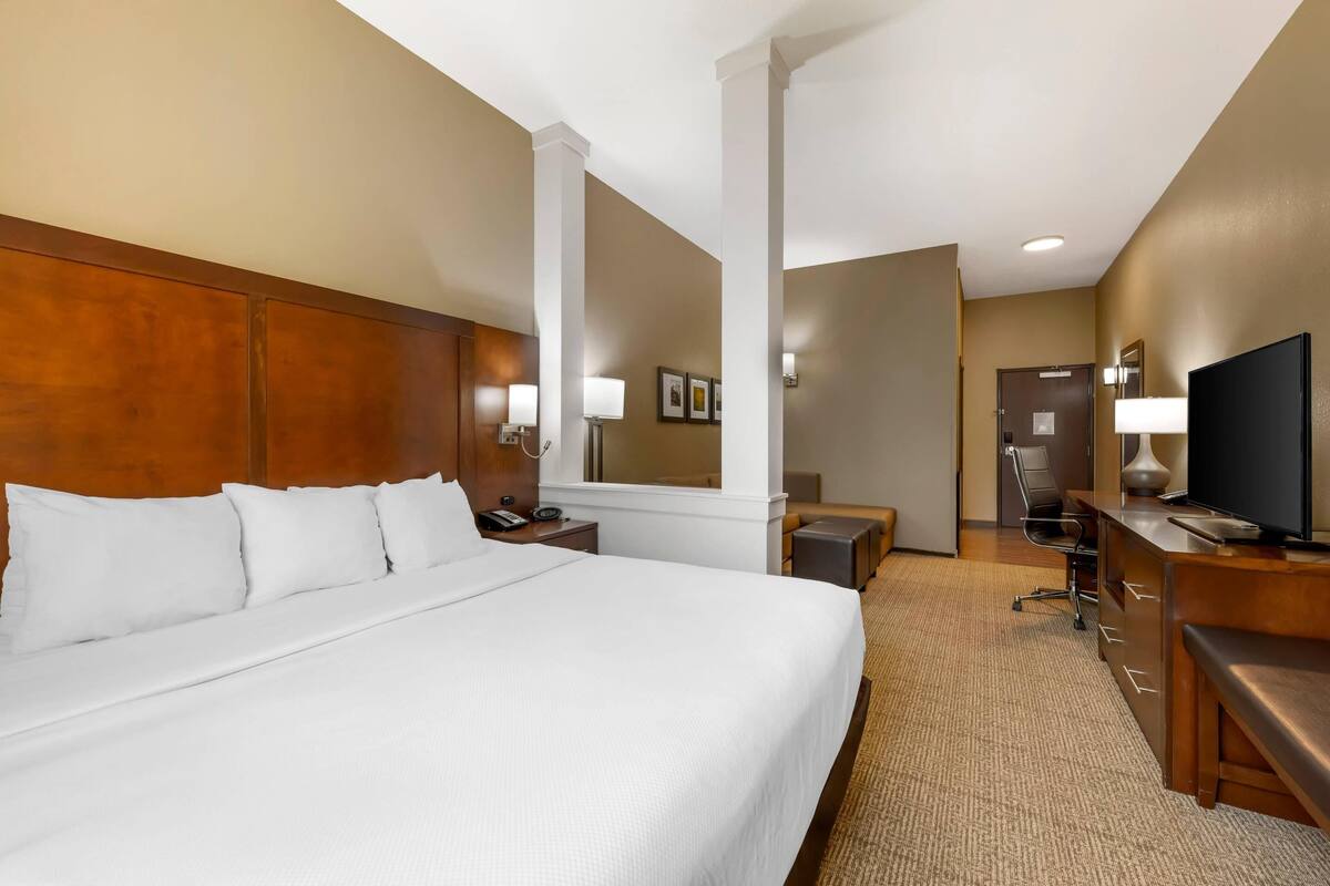 A hotel room with a large bed, a desk with a television, a chair, and a small table.