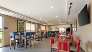 Un vaste espace dédié à la salle à manger, avec de nombreuses tables et chaises, de grandes fenêtres et un téléviseur à écran plat fixé au mur.