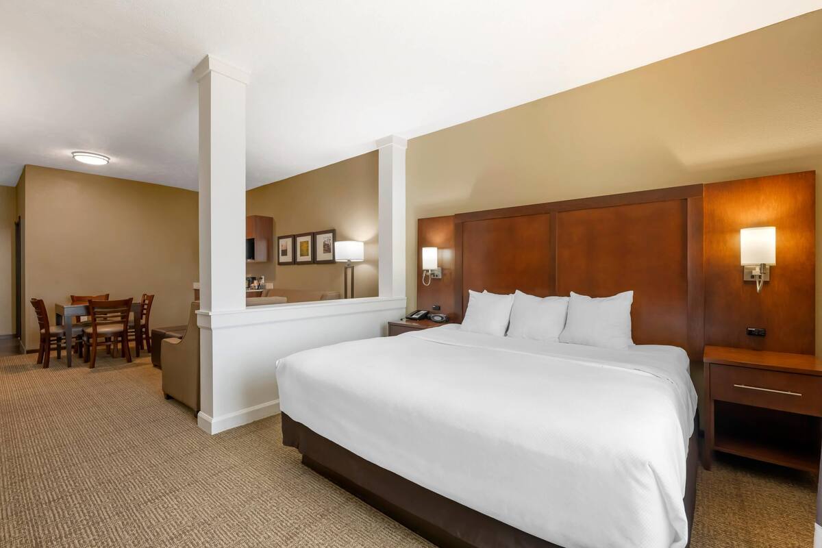 A hotel room with a large bed, a desk with a chair, a small table, and a mirror.