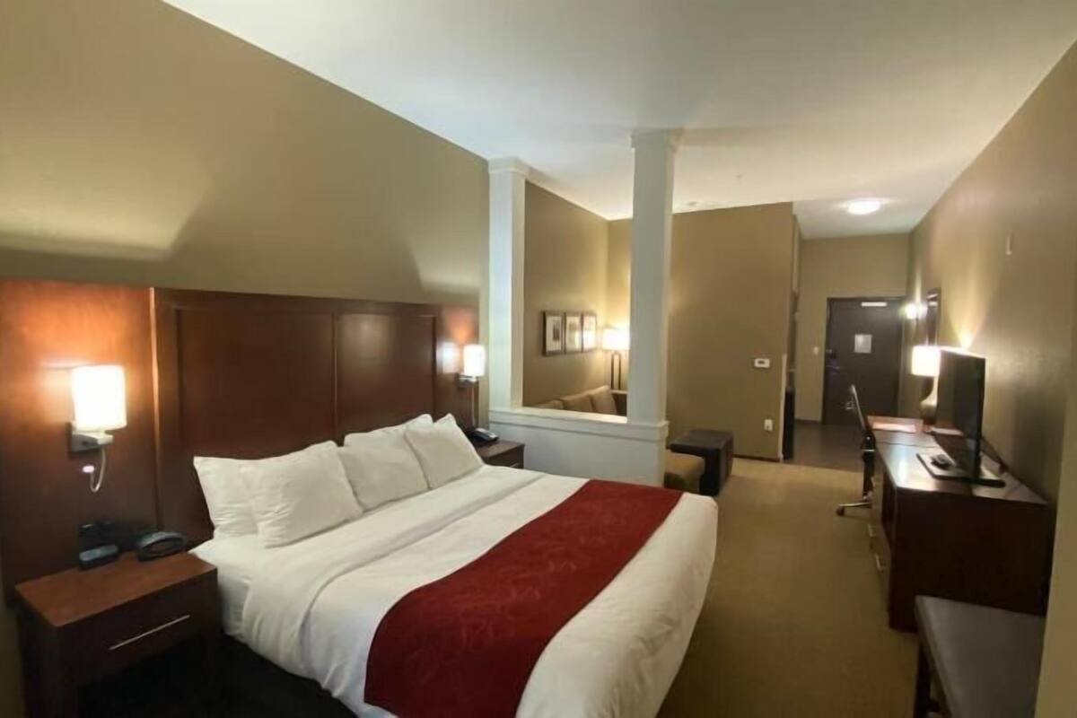 A hotel room with a bed, bedside tables, a desk, a chair, a TV, and a mirror.