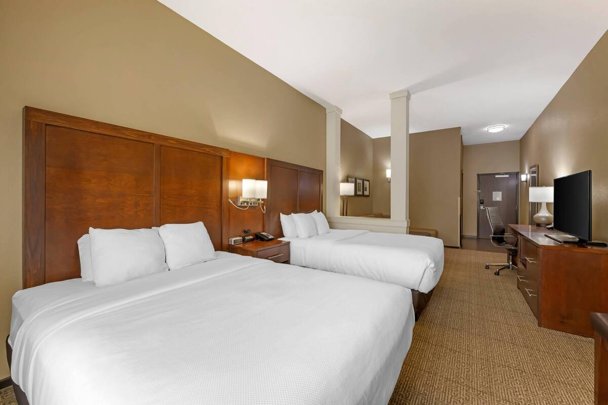 A hotel room with two beds, a desk, a chair, a TV, and a mirror.