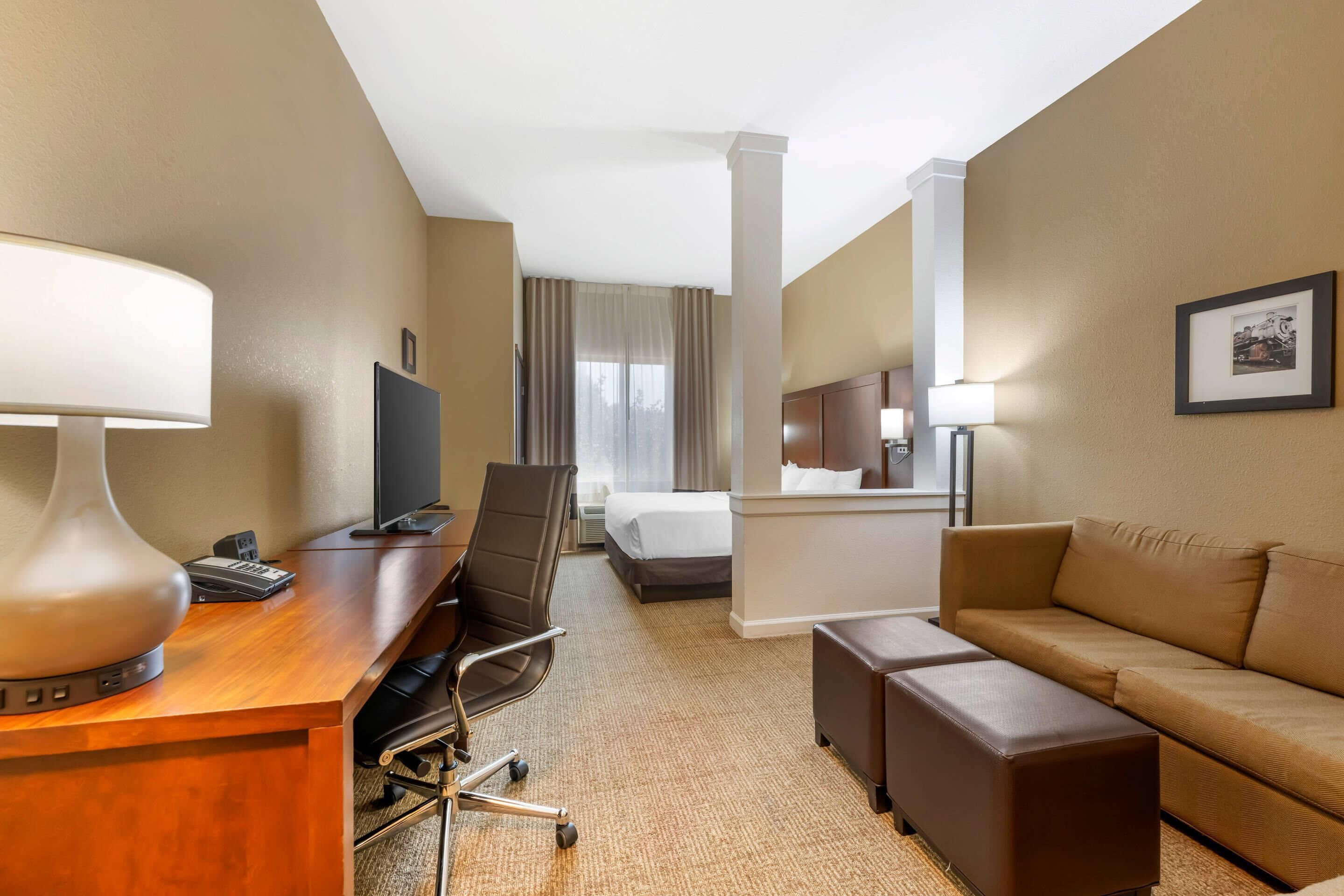 Quarto de hotel com secretária de madeira, uma cadeira, um sofá, uma cama e uma televisão.