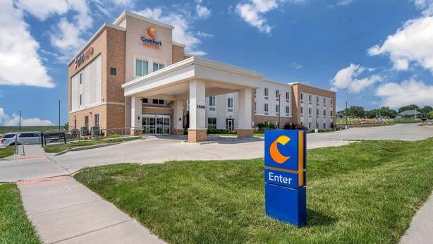 Un hôtel Comfort Suites avec une entrée bien visible, un panneau indiquant l’entrée et un parking avec des voitures.