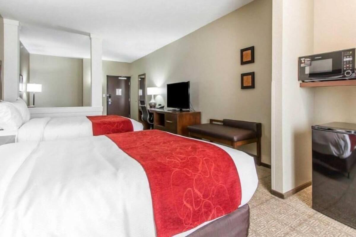 A hotel room with two beds, a TV, a desk, a chair, and a microwave.