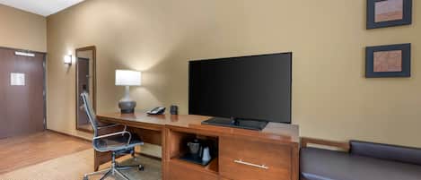 Habitación de hotel con un escritorio de madera, una silla negra, un televisor, un sofá y piso alfombrado.