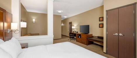 Habitación de hotel con una cama grande, un escritorio con silla, televisión, armario y espejo.