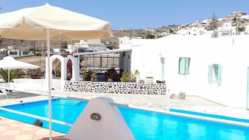 A swimming pool with a tiled deck, a lounge chair, and a sun umbrella.
