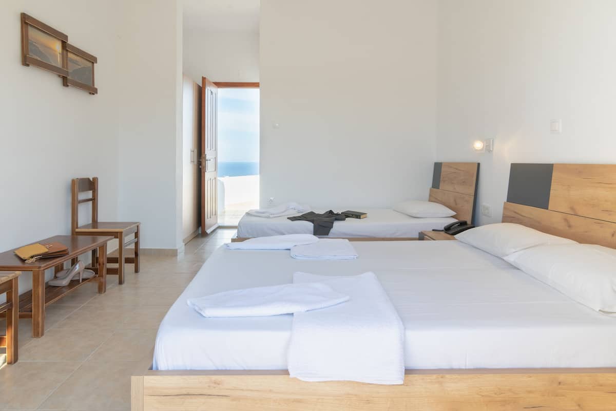 A hotel room with two beds, a wooden desk, a chair, and a view of the sea.