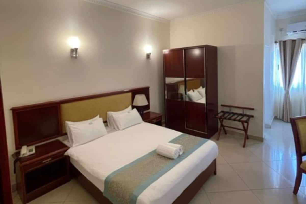 A hotel room with a large bed, bedside tables, a wardrobe, a desk, and a chair.