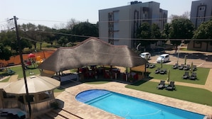 A swimming pool with a thatched-roof pavilion, lounge chairs, and a children's play area. - The Matola Hotel (Matola)