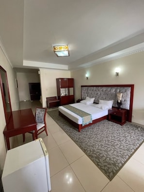 A hotel room with a bed, bedside tables, a desk, a chair, and a wardrobe.