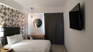 A hotel room with a bed, a desk, a flat-screen TV, a wall-mounted lamp, and a geometric-patterned wall. - Urbainn Hotel (Veracruz)