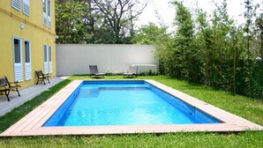 A rectangular swimming pool with a wooden deck surrounding it, two lounge chairs, and a yellow building with shutters in the background. - Urbainn Hotel (Veracruz)