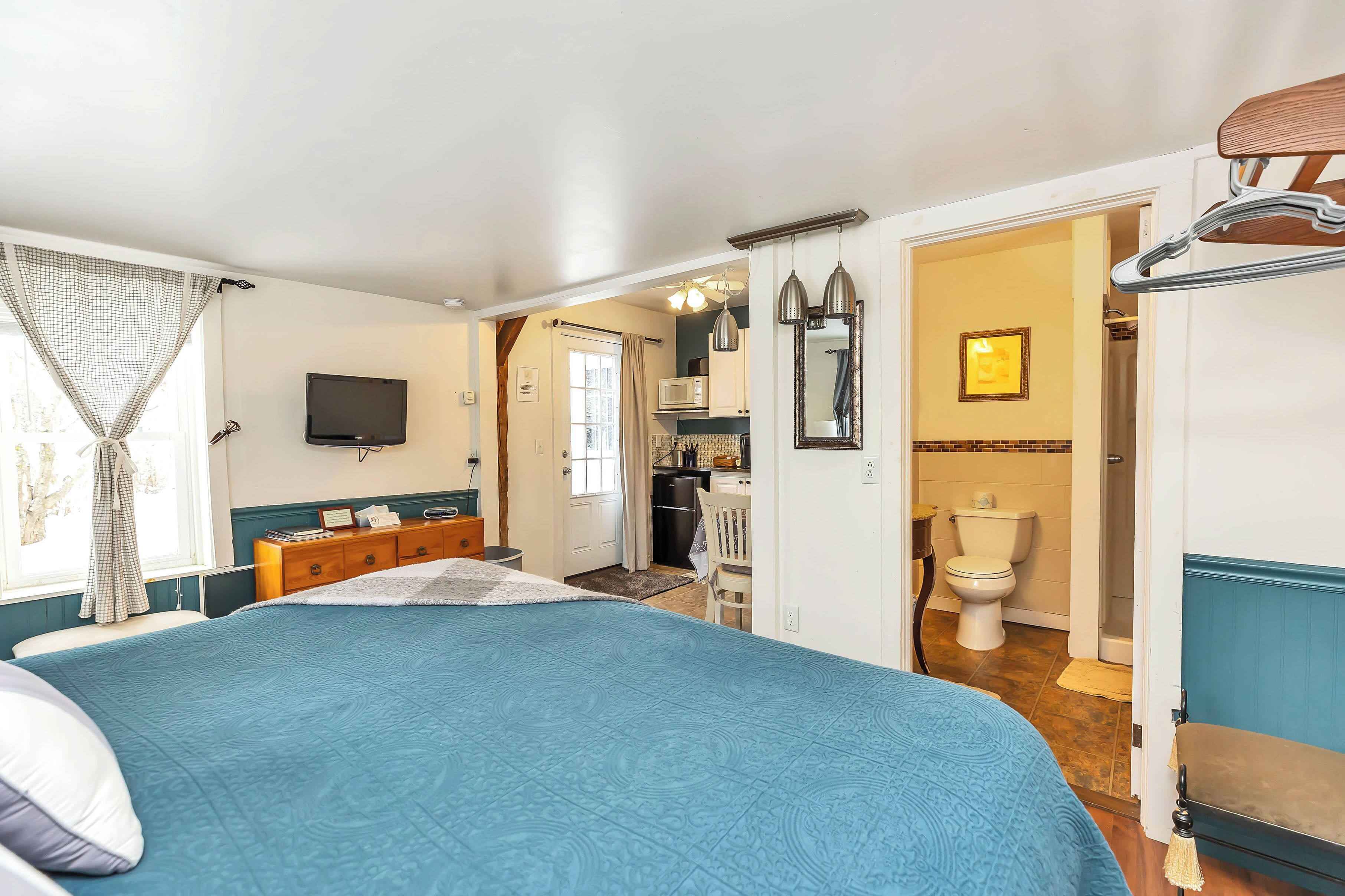 A bedroom with a large bed, a dresser, a television, and a bathroom visible through an open door.