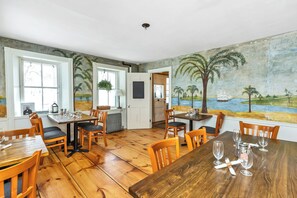 A dining area with wooden tables and chairs, a mural on the wall, and large windows. - The Birchwood Inn (Temple)