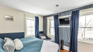 A bedroom with a bed, two windows, a television, and a chair.