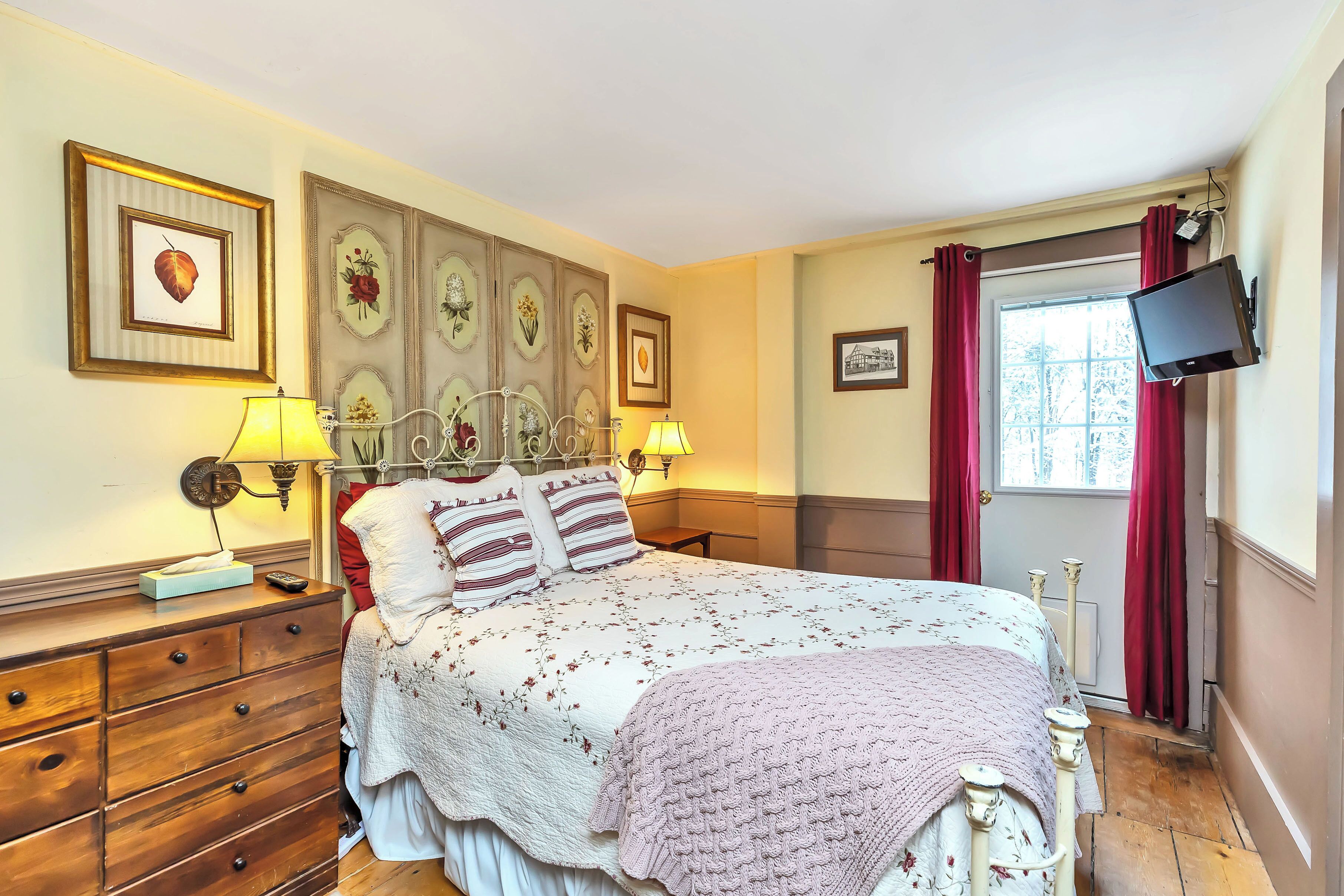 A bedroom with a bed, wooden dresser, wall-mounted lamps, and a television.
