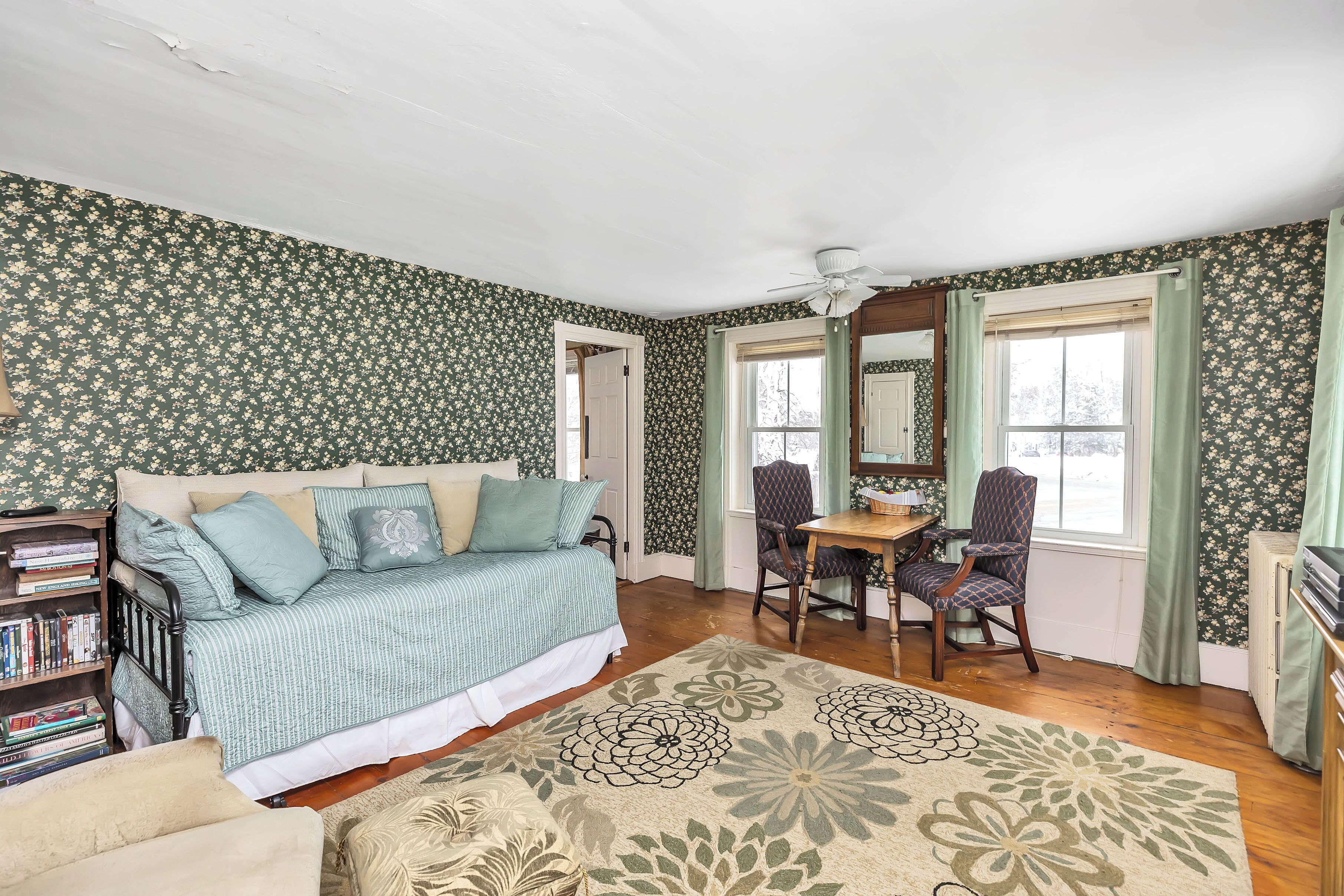 A bedroom with a bed, a desk, a chair, a bookshelf, and a large window.