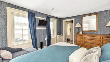 Ein Schlafzimmer mit einem großen Bett, einem Schminktisch, einem Fernseher und einem Fenster mit Vorhängen.