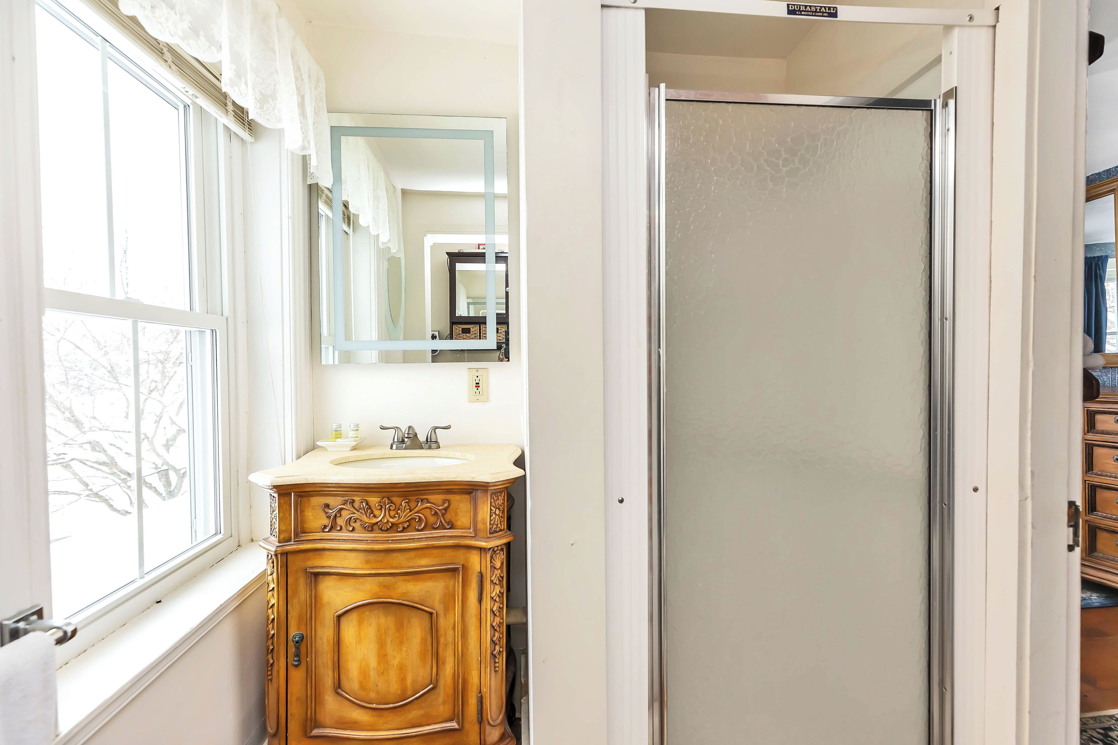 A bathroom with a wooden vanity, a mirror, and a frosted glass door.