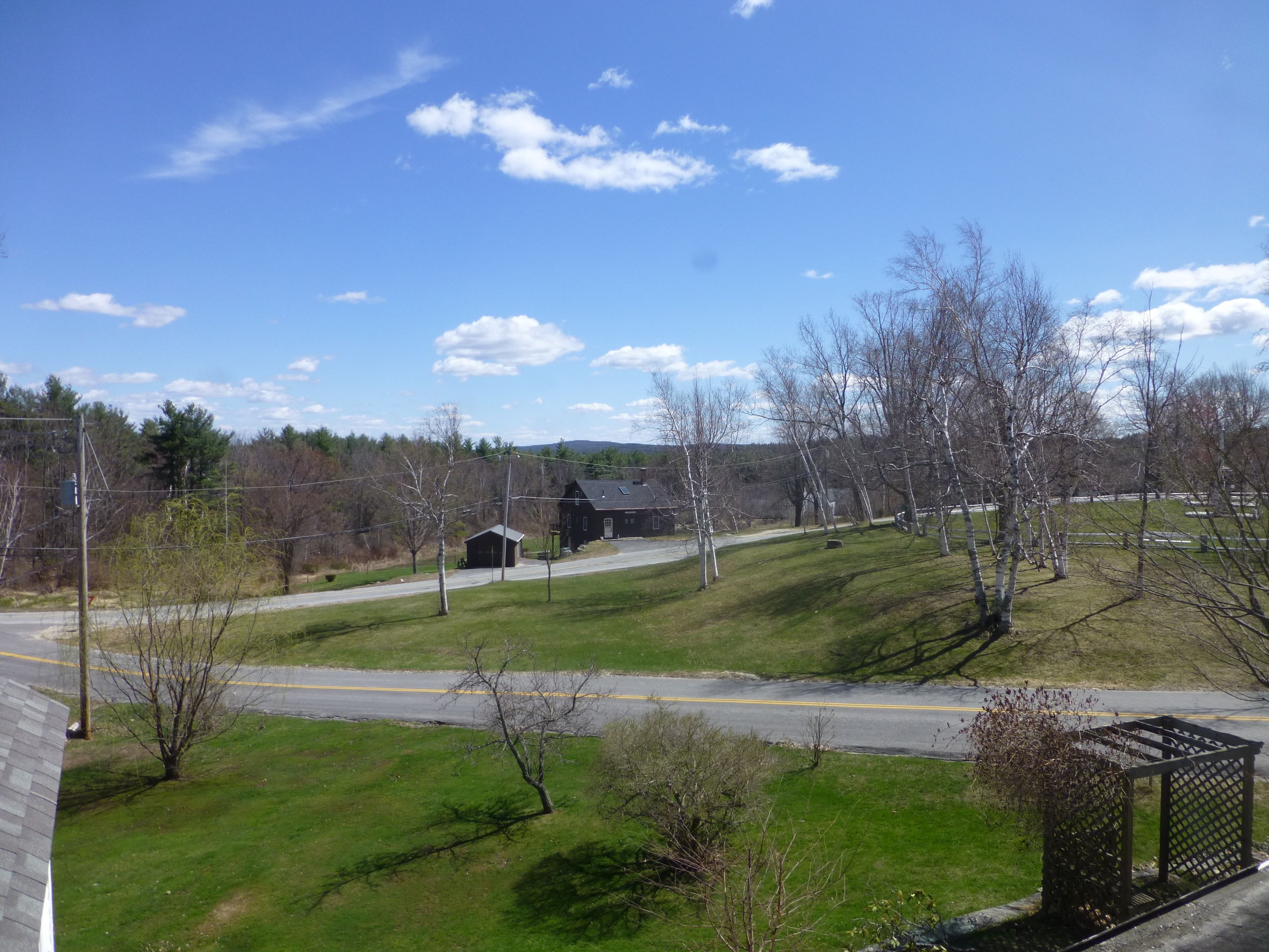 A rural landscape with a road, a small building, and trees.