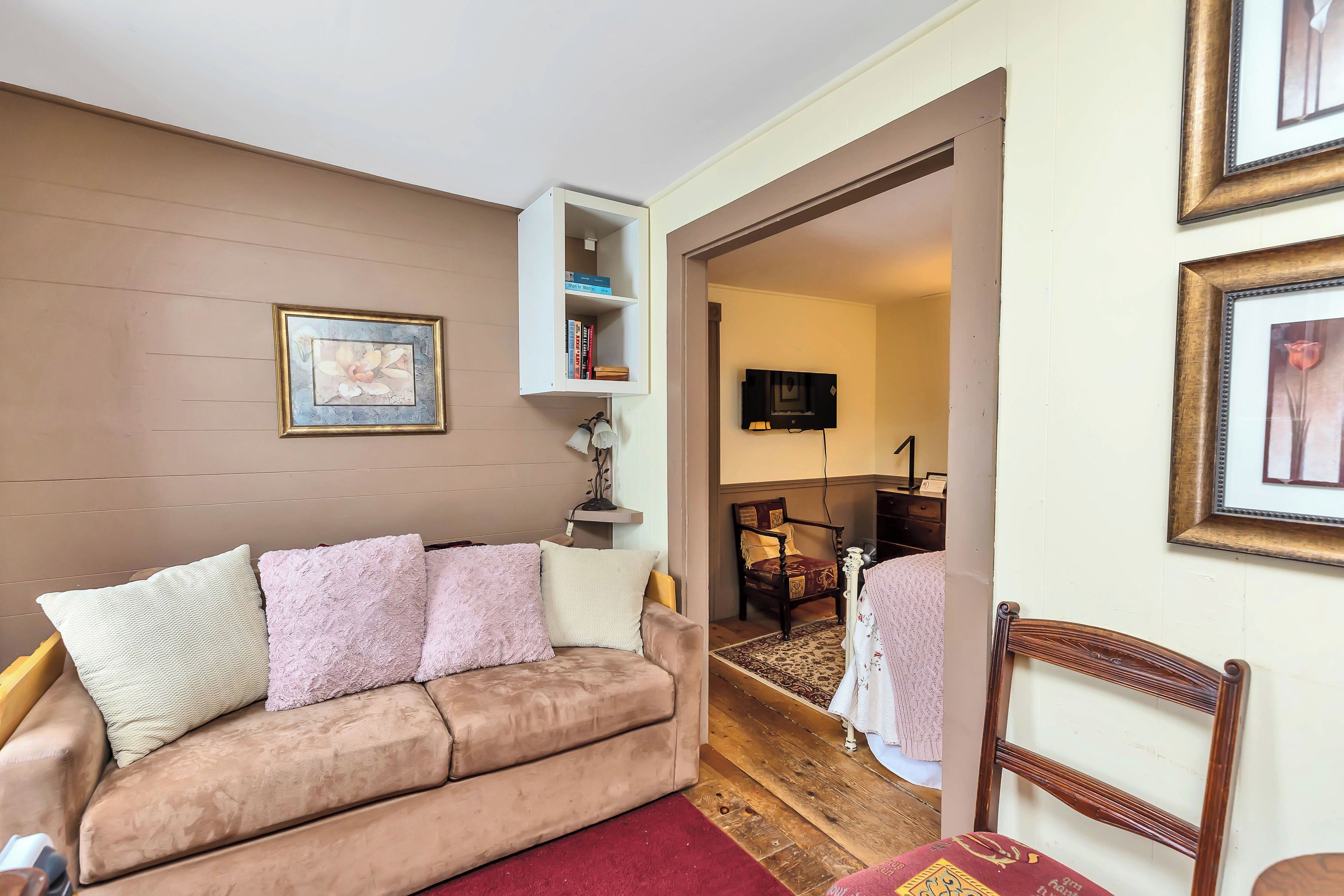 A cozy living room with a brown sofa, a small white shelf, and a wooden chair.