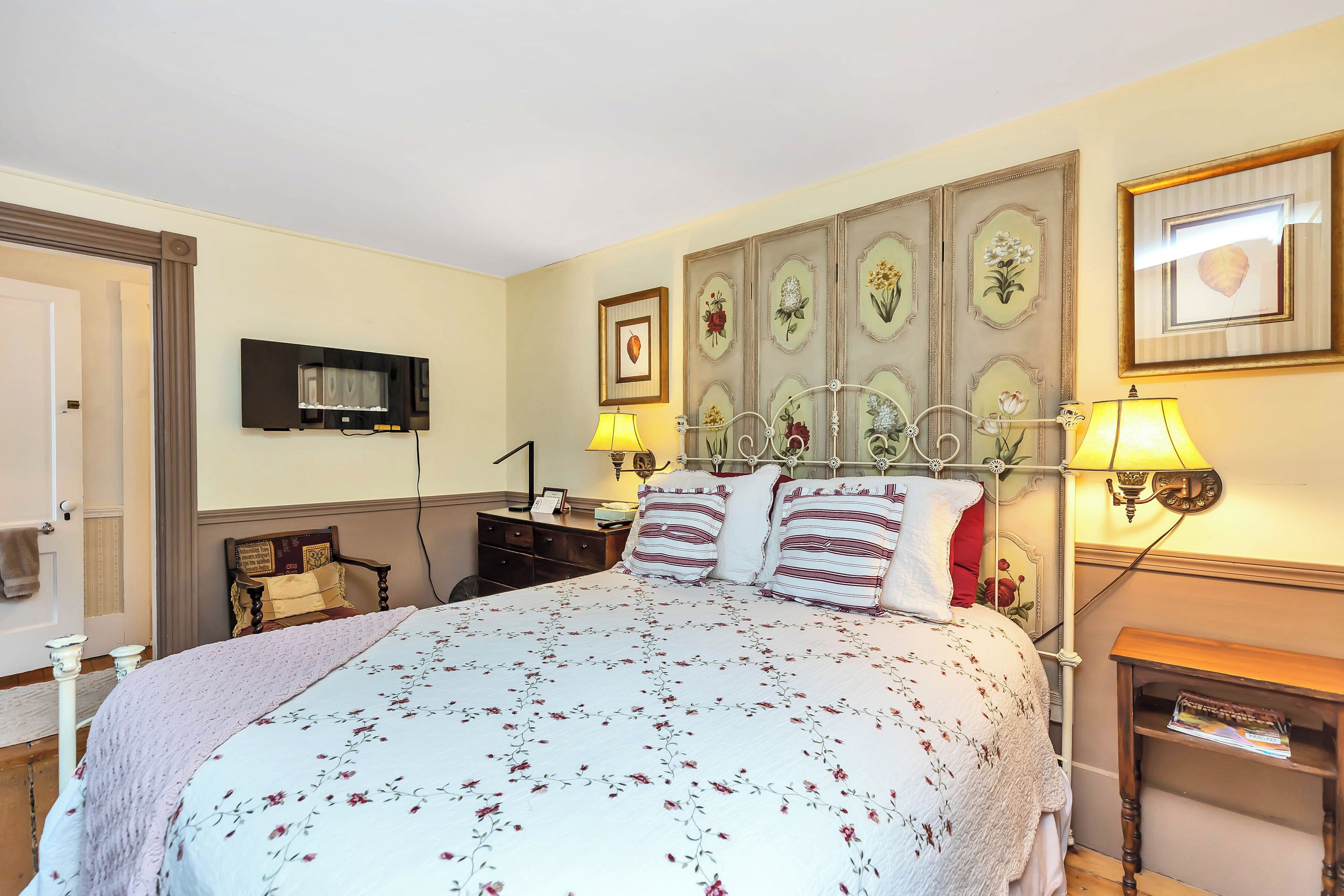 A neatly arranged bedroom with a large bed, bedside tables, a television, and decorative wall art.