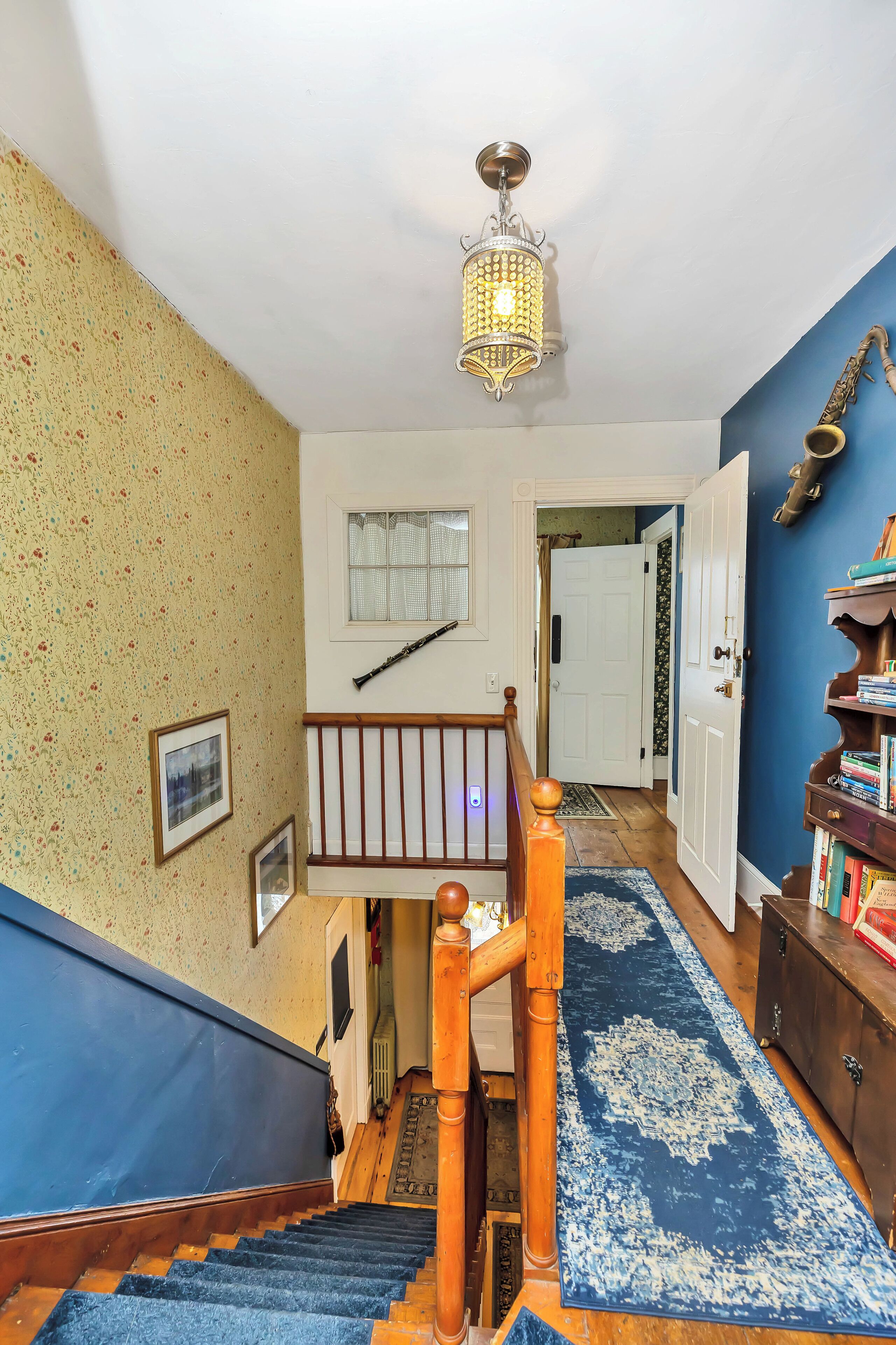 A staircase with a blue carpet, wooden handrail, and a hanging light fixture.
