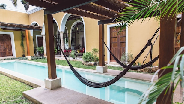 Un área de piscina con una hamaca, un porche cubierto y un edificio con puertas arqueadas.
