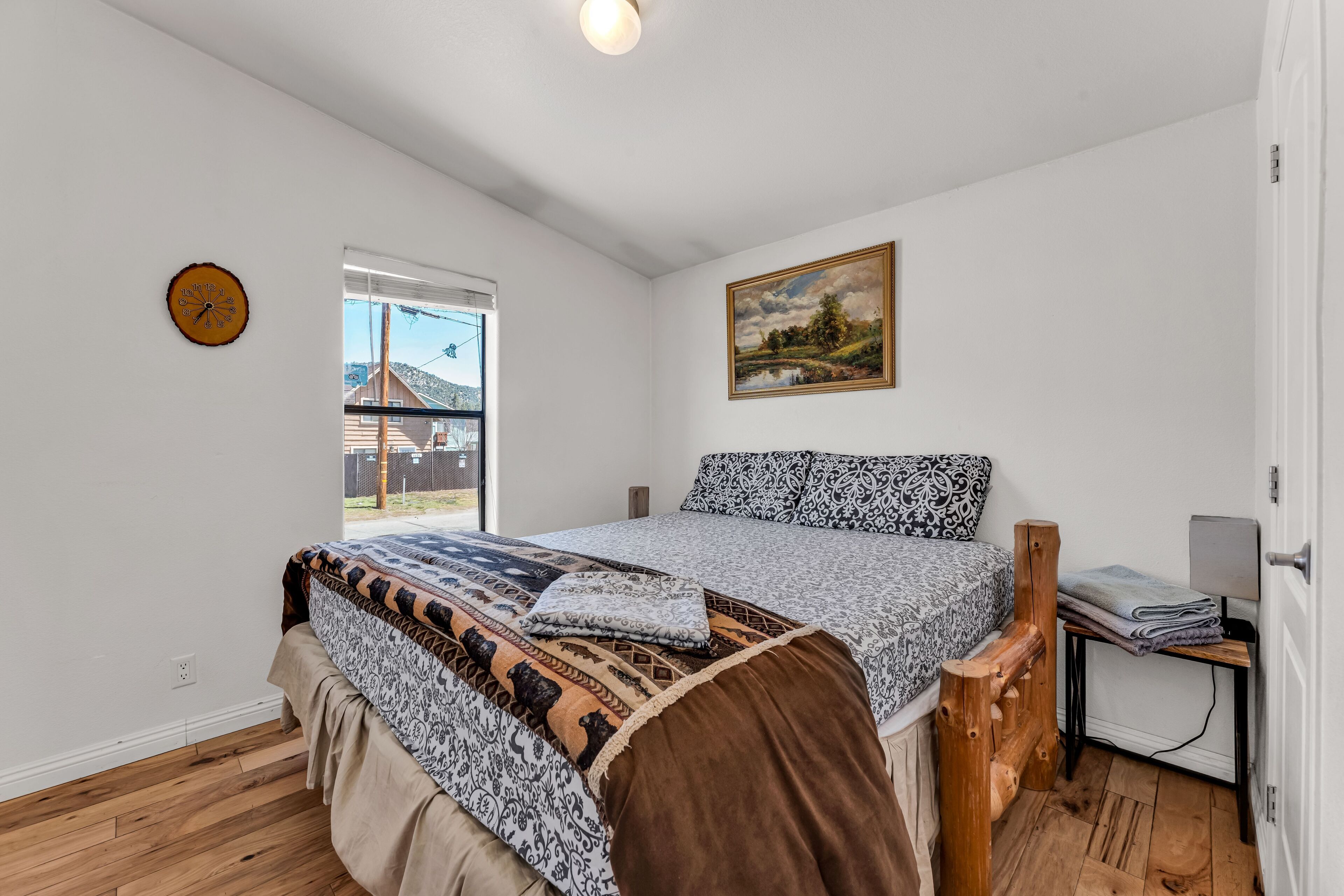 A bedroom with a bed, a window, a clock, and a painting on the wall.