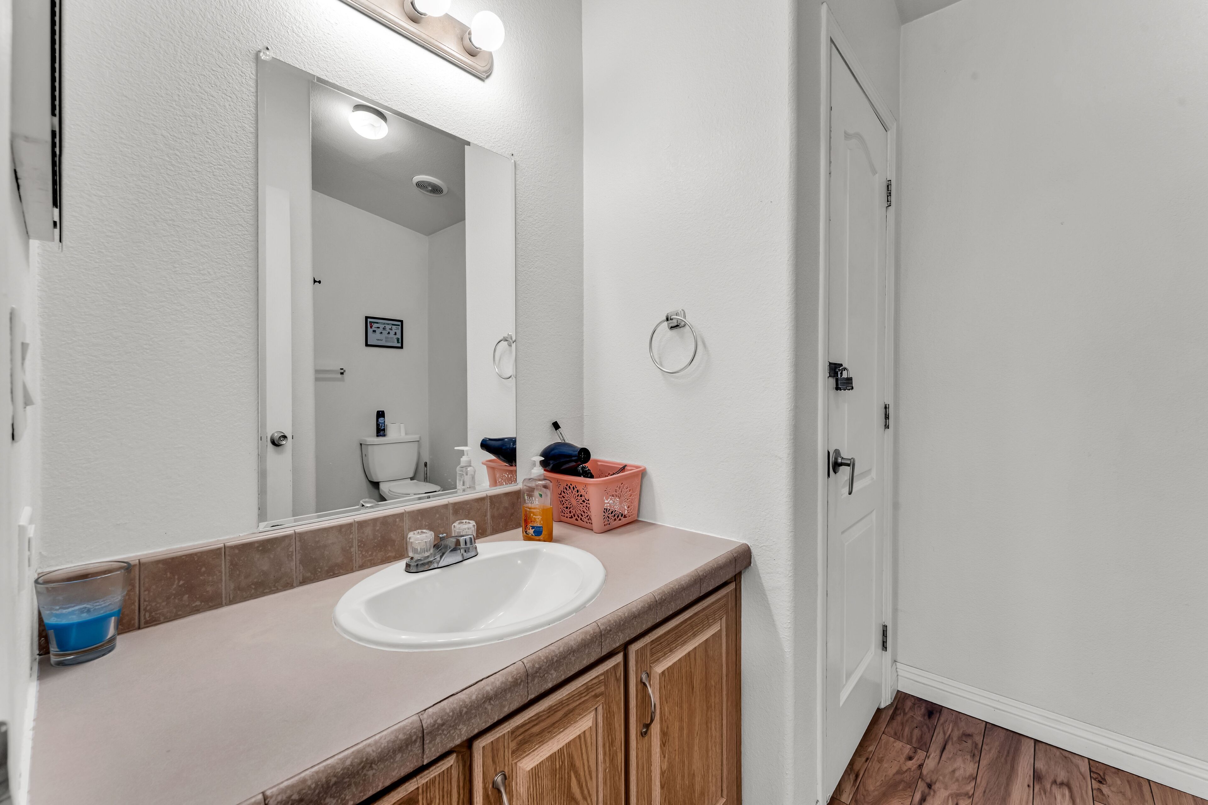 A bathroom with a white sink, wooden cabinets, a mirror with lights, and a door.