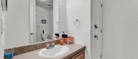 A bathroom with a white sink, wooden cabinets, a mirror with lights, and a door.