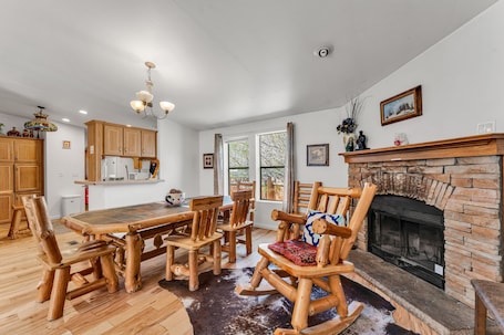A spacious dining area with a wooden table and chairs, a fireplace, and a kitchen in the background.