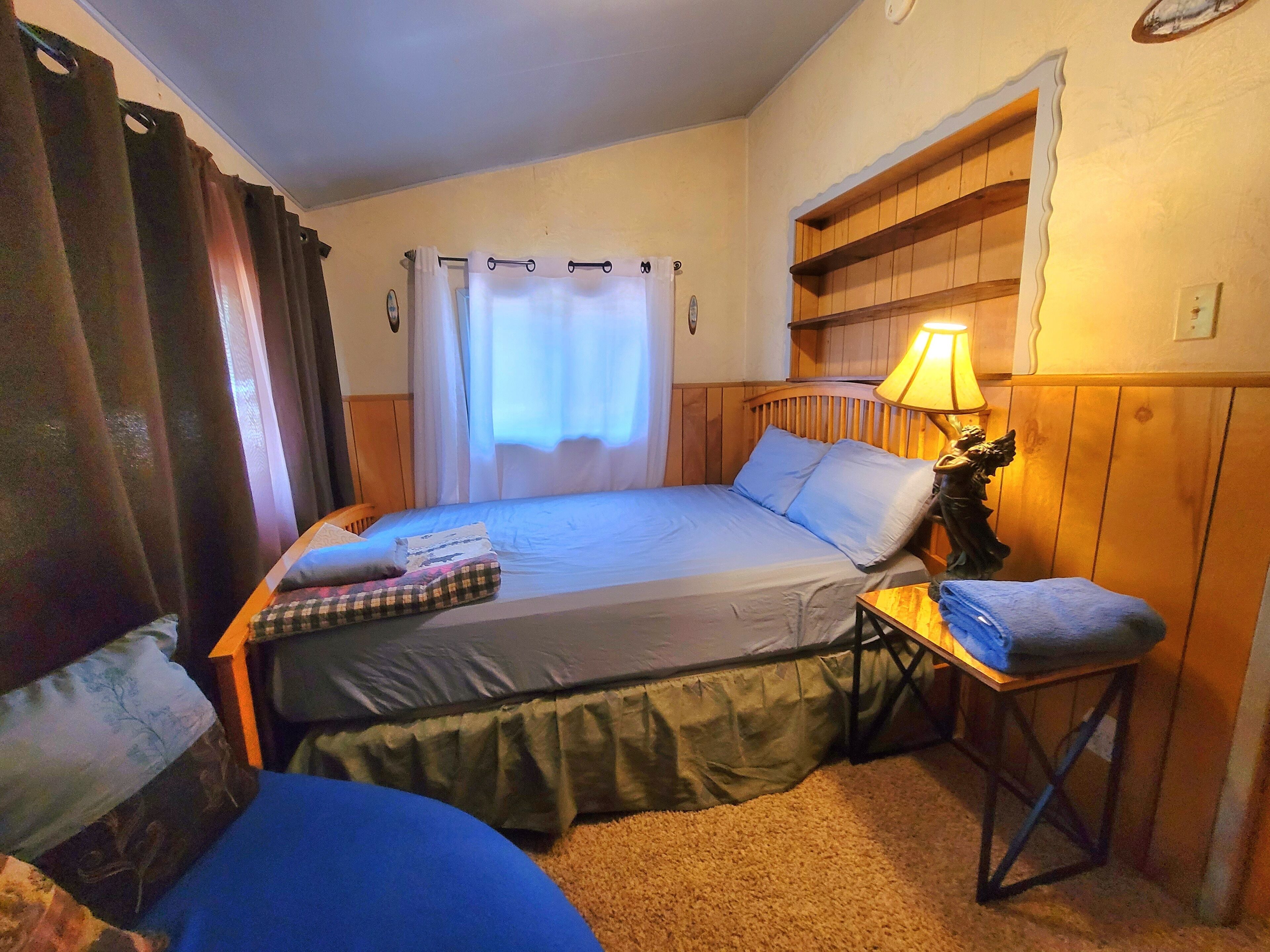 Une chambre à coucher avec un lit, une table de chevet avec une lampe, une chaise et une petite étagère.