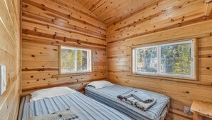 A cabin room with two beds, wooden walls, and windows with blinds. - Myrtle Chalet (Big Bear City)