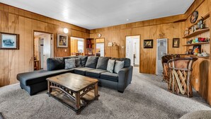 A cozy living room with a sectional sofa, a wooden coffee table, and a bar area with stools. - Myrtle Chalet (Big Bear City)
