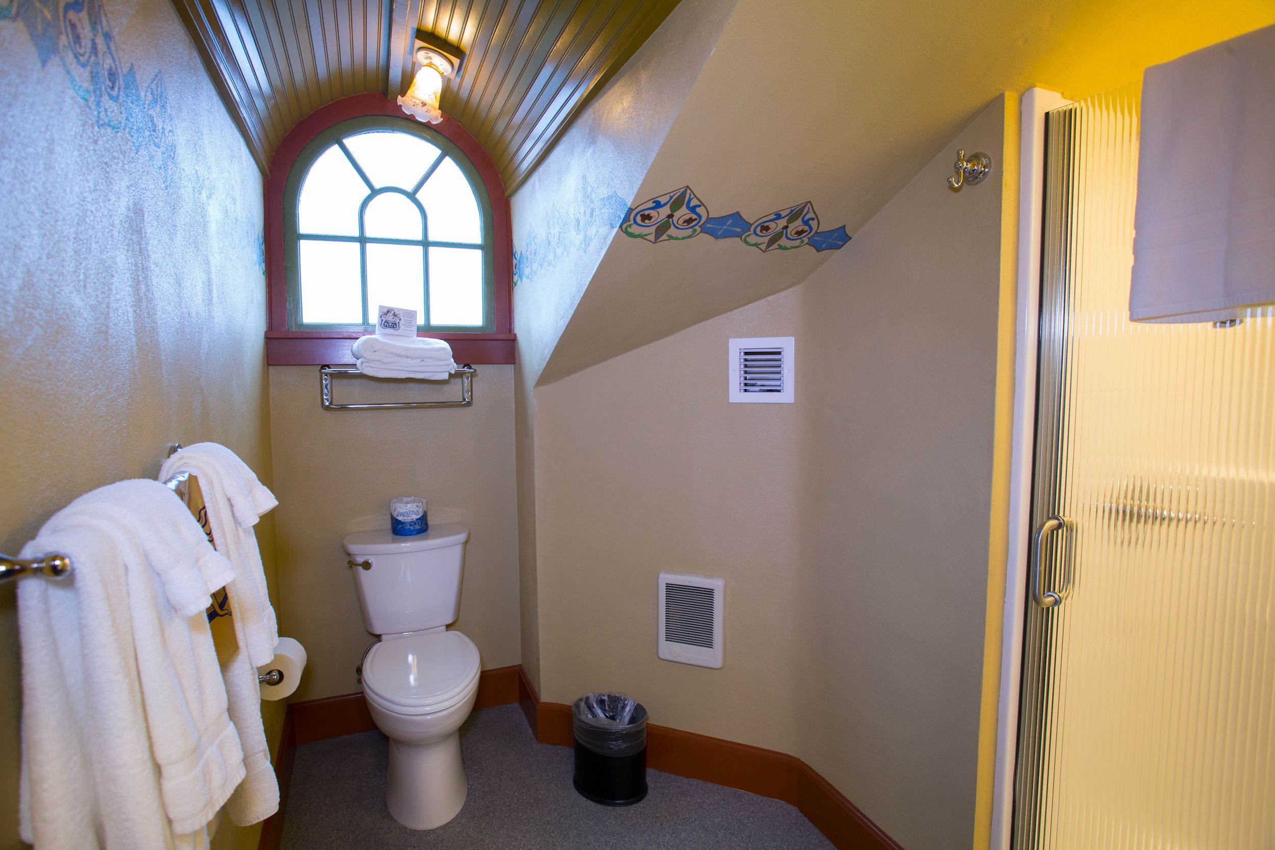 A bathroom with a toilet, a towel rack, a window, and a shower door.