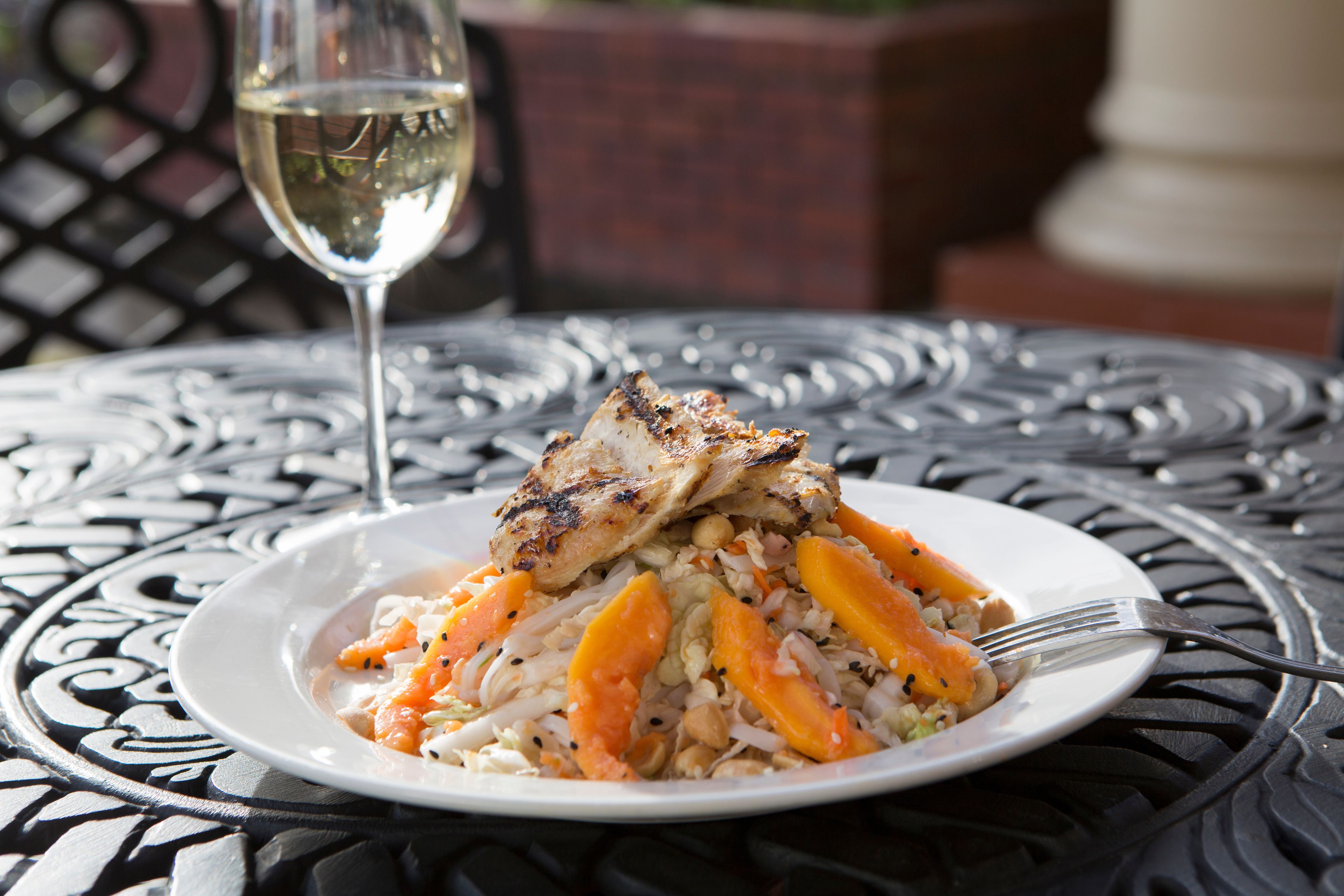A plate of food with grilled chicken and vegetables on a metal table.