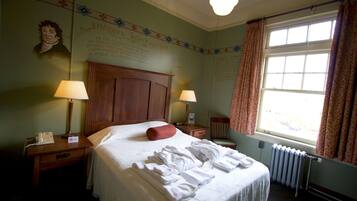 A hotel room with a large bed, two bedside tables with lamps, a window with curtains, and a wall with a portrait and text.