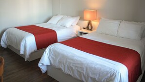 Dos camas individuales con ropa de cama blanca y roja, una mesita de noche con lámpara, y suelo de madera.