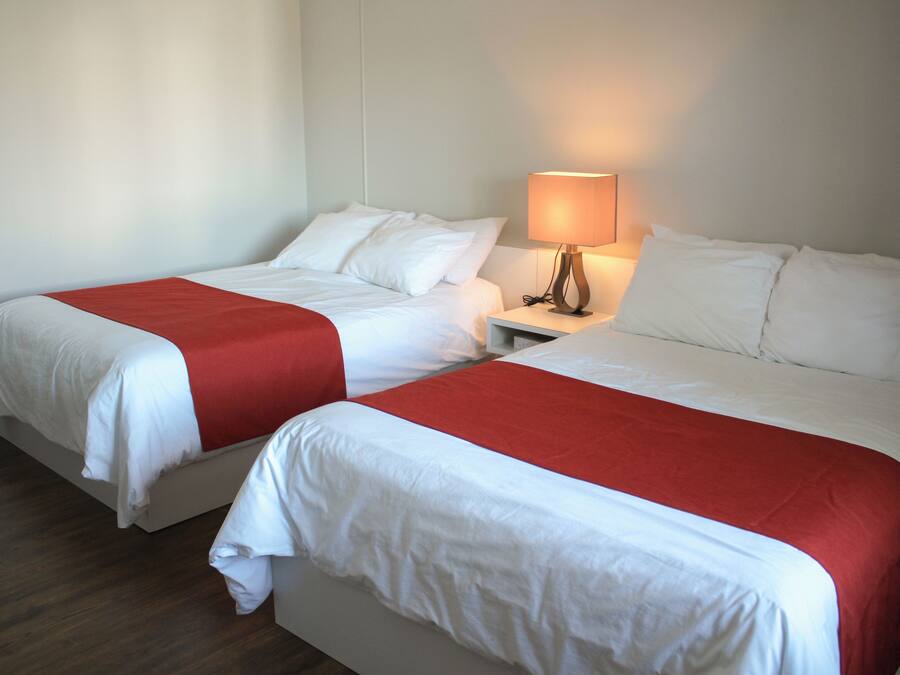 Two single beds with white and red bedding, a bedside table with a lamp, and a wooden floor.