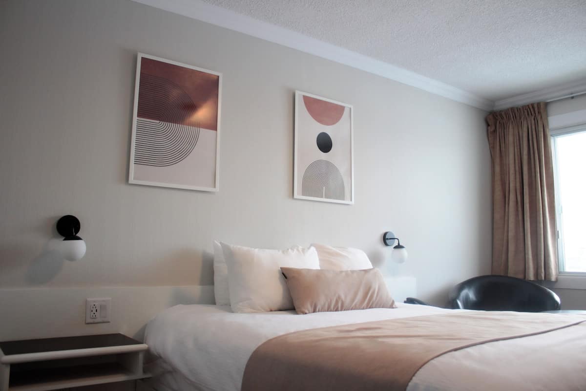 A hotel room with a bed, a desk, and two wall-mounted light fixtures.