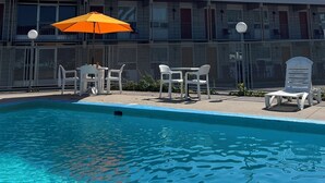 Una piscina con sillas de descanso blancas y un paraguas naranja.