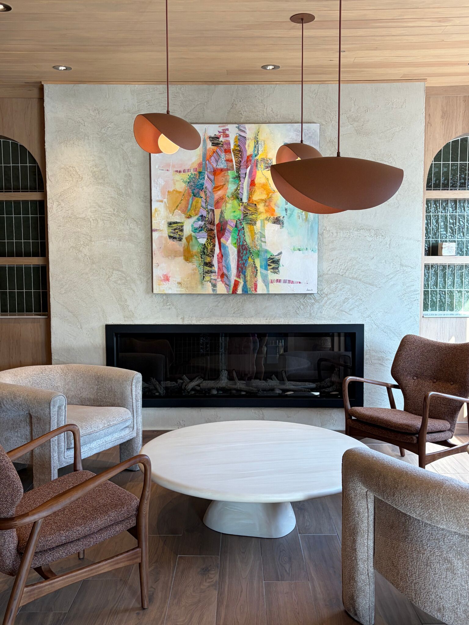 A modern living room with a fireplace, two armchairs, a round coffee table, and a colorful abstract painting above the fireplace.
