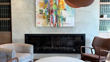 A modern living room with a fireplace, two armchairs, a round coffee table, and a colorful abstract painting above the fireplace.