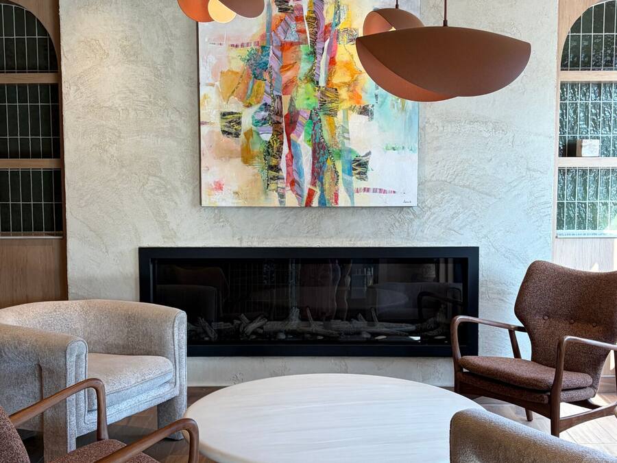 A modern living room with a fireplace, two armchairs, a round coffee table, and a colorful abstract painting above the fireplace.