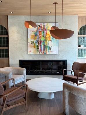 A modern living room with a fireplace, two armchairs, a round coffee table, and a colorful abstract painting above the fireplace. - Auberge Le Parasol  (Saguenay)