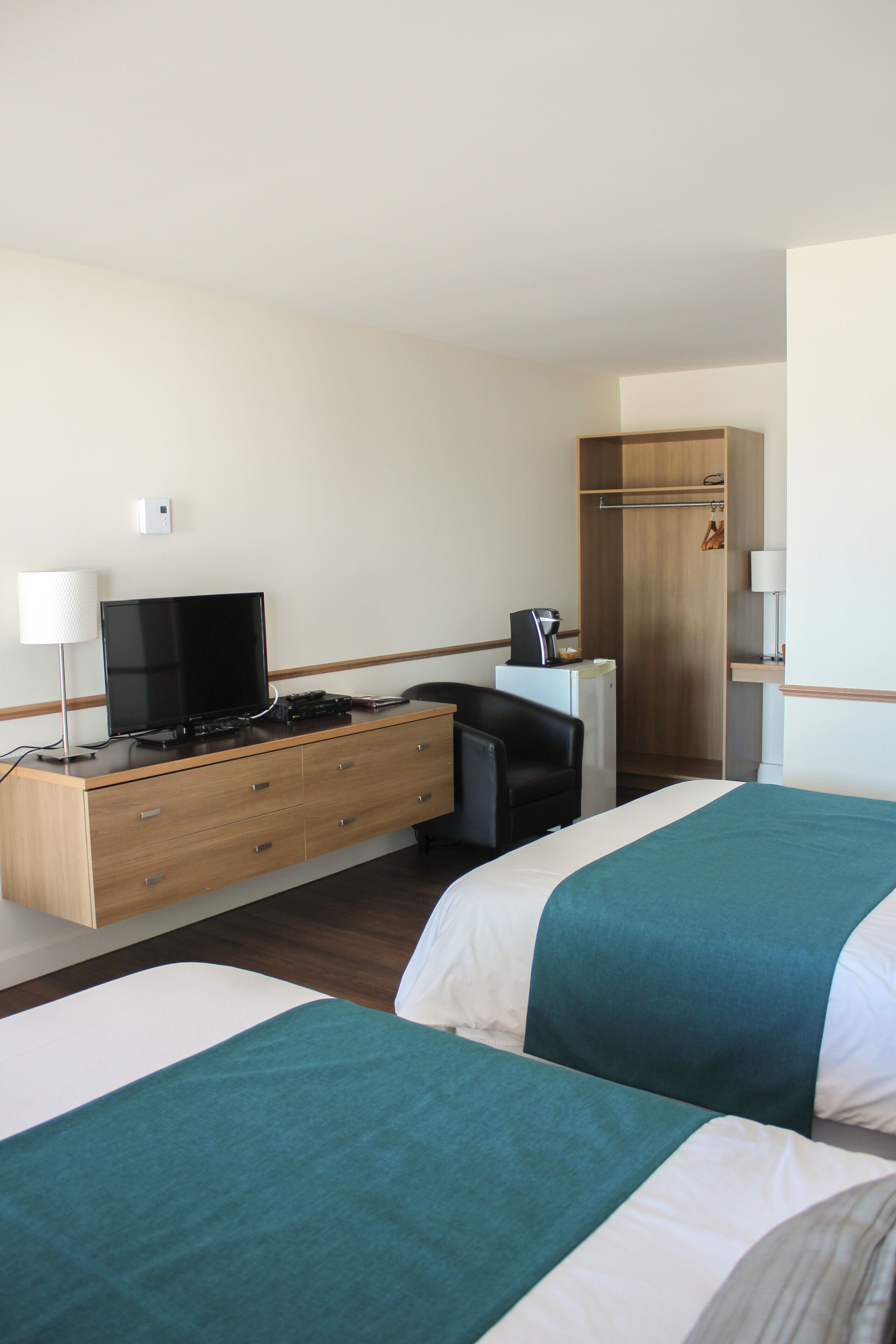 Habitación de hotel con dos camas, un escritorio, televisor, cafetera y armario.