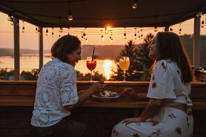 Two people seated at a table with drinks and a view of the sunset. - Auberge Le Parasol  (Saguenay)